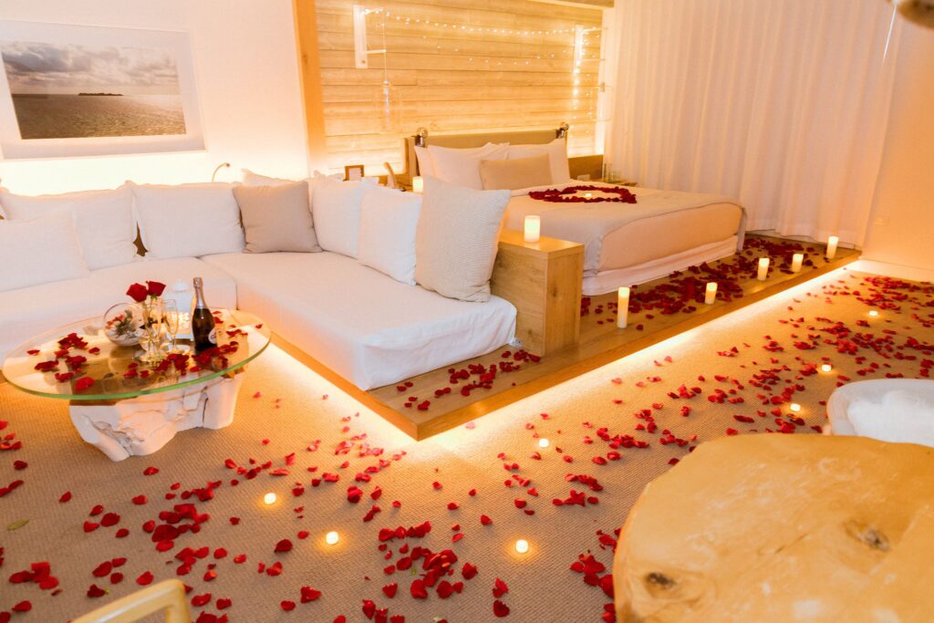 Romantic hotel suite with candles, rose petals, lounge seating, and soft ambient lighting